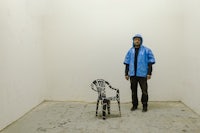 a man in a blue jacket standing next to a chair